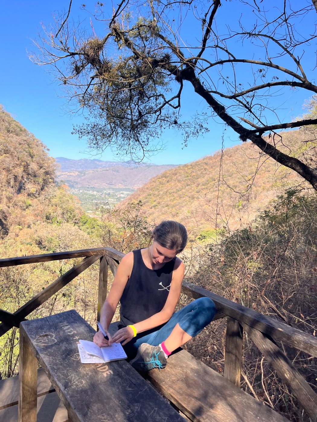 Natasha Rondy writing in a notebook in a natural outdoor setting.