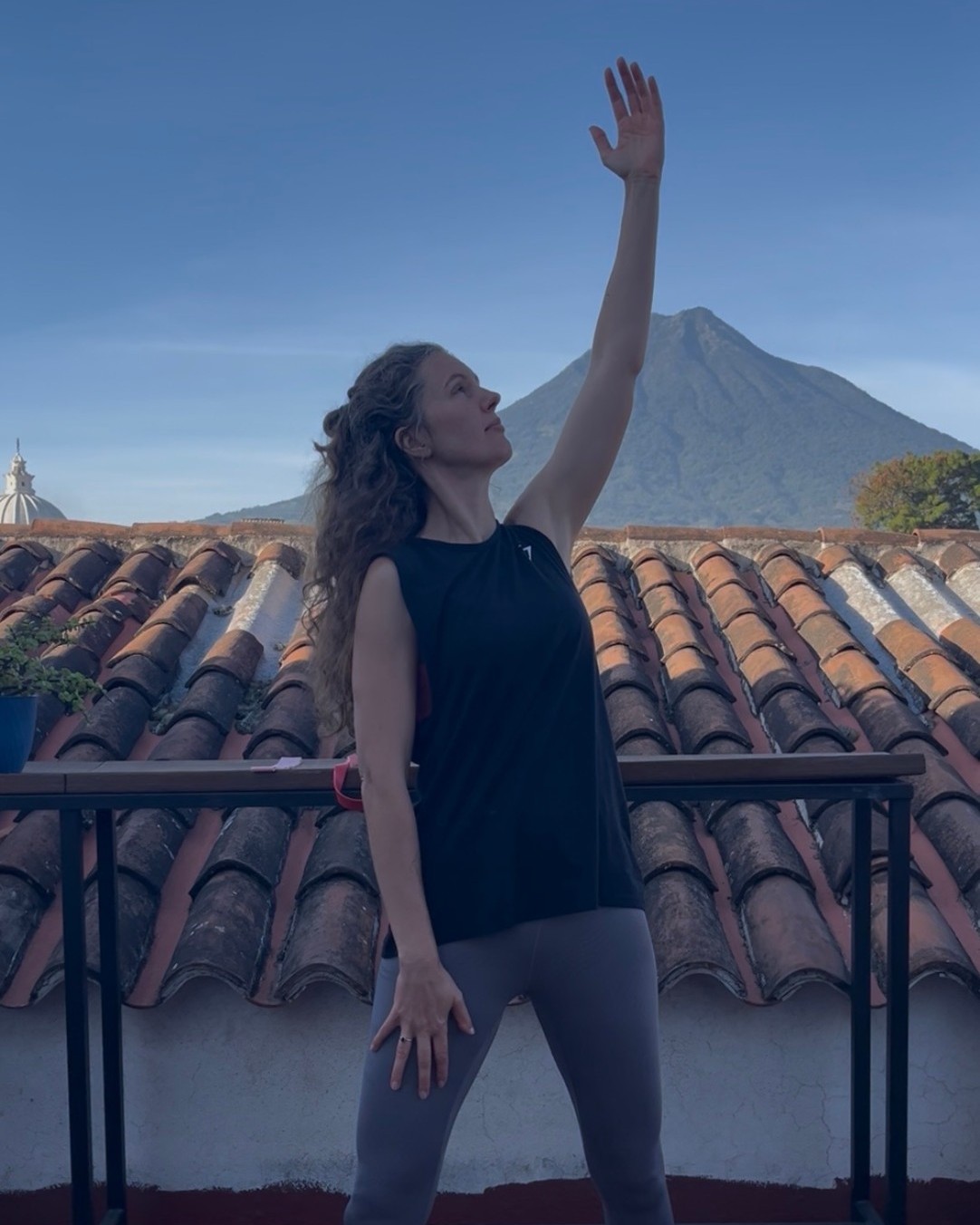 Natasha Rondy moving on a rooftop in Antigua, Guatemala, one arm reaching towards the sky with a volcano beyond
