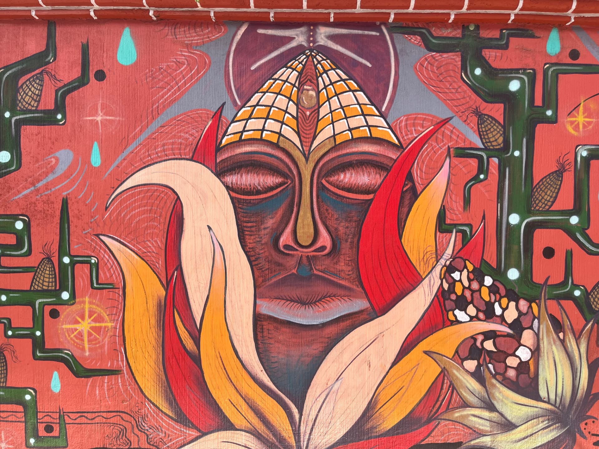 A painted mural of a serene face with closed eyes crowned with maize, Mexico
