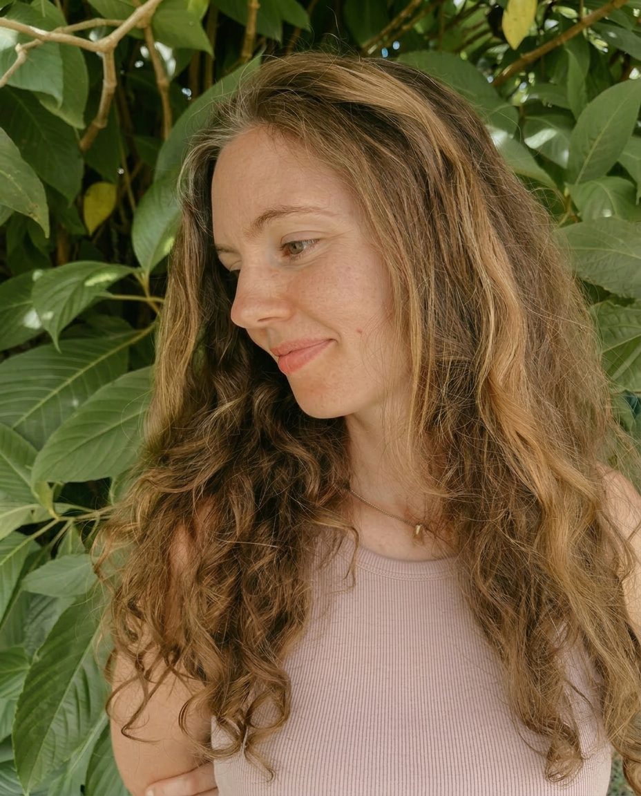 A quiet portrait of the founder among soft green leaves, looking gently downward in natural light