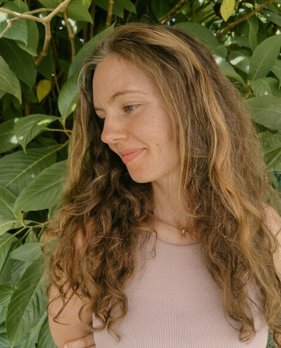 A quiet portrait of the founder among soft green leaves, looking gently downward in natural light